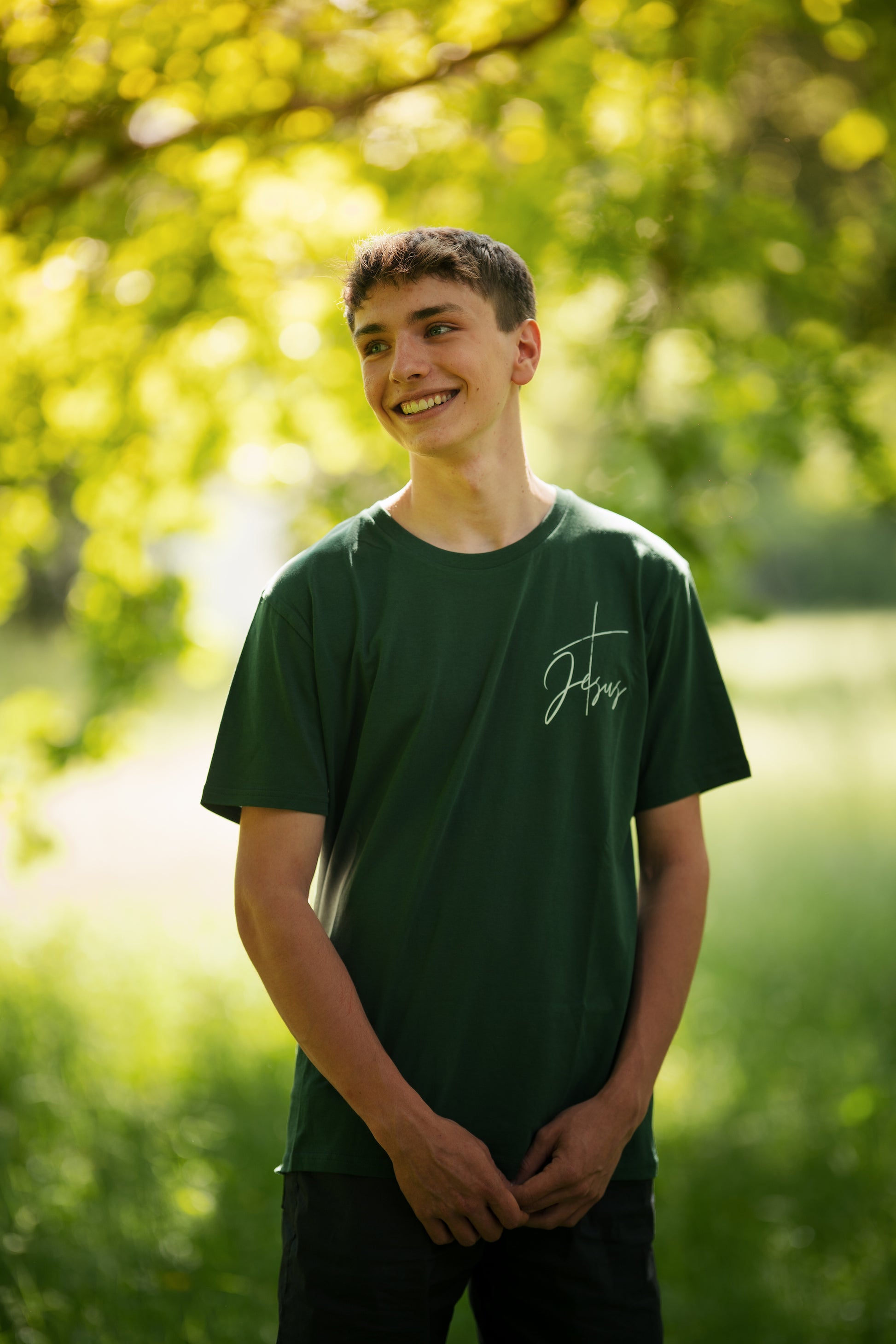 christliches T-Shirt mit einem Unisex-Schnitt an einem Model in grün aus 100 % Bio-Baumwolle "Kreuz Jesus" mit einem Kreuz und dem Schriftzug Jesus rechts (minimalistisch) auf der Brust. Erhältlich in den Größen S bis XXL